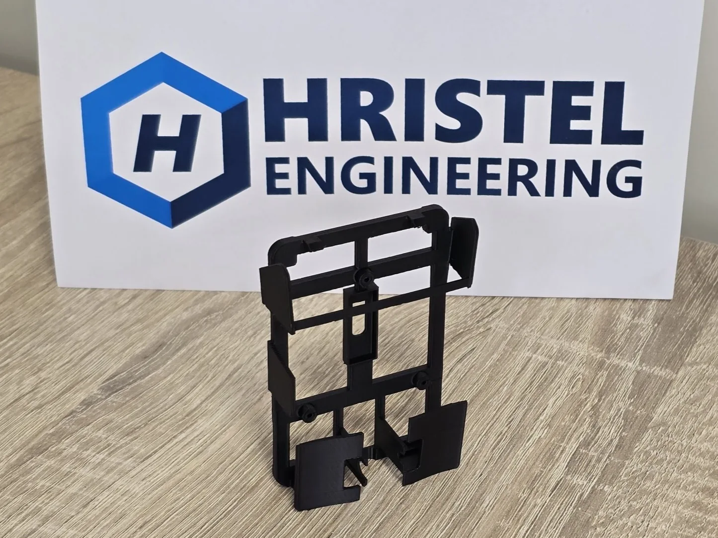 Black 3D printed frame in front of the HRISTEL logo