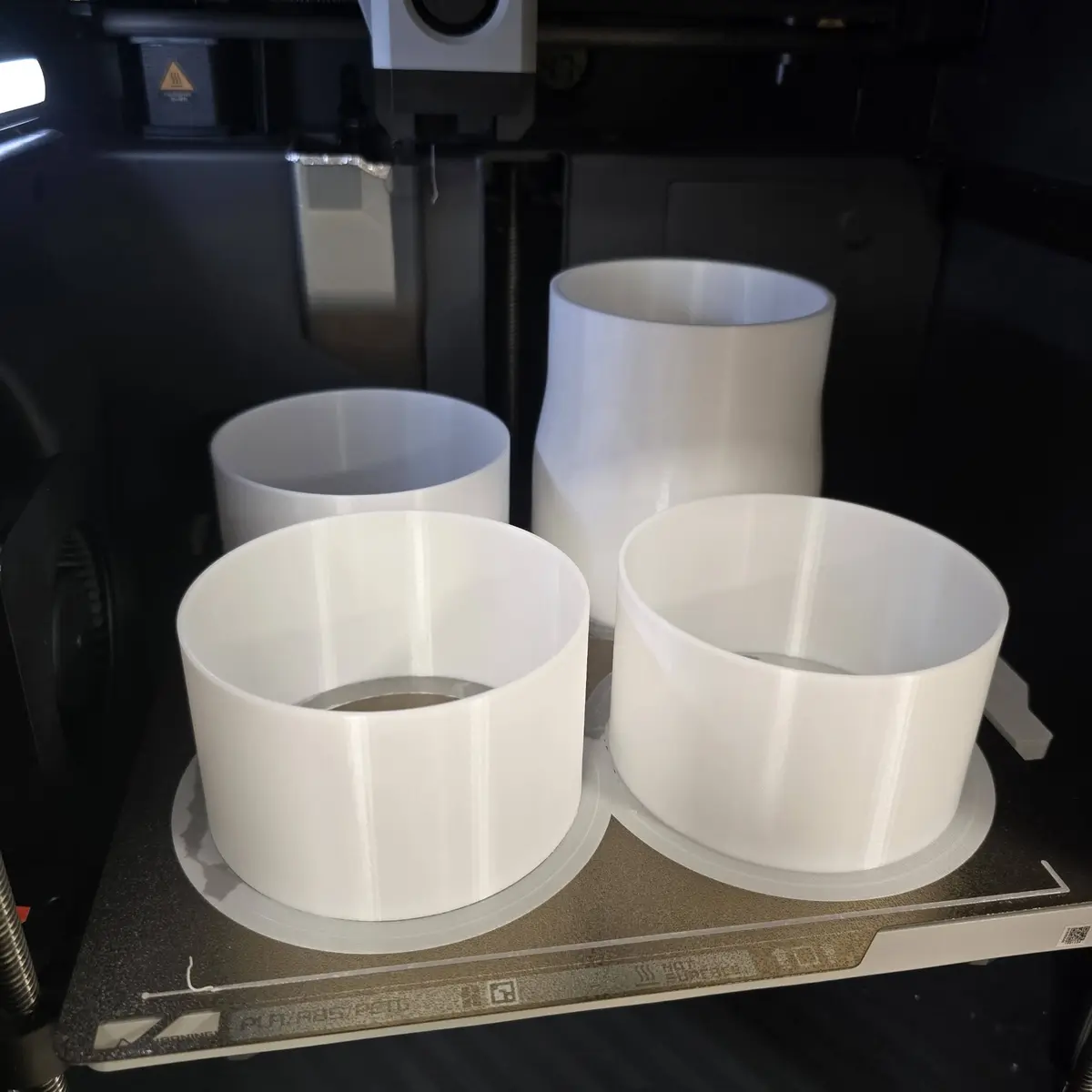 Four white cylindrical 3D printed parts on a printer build plate